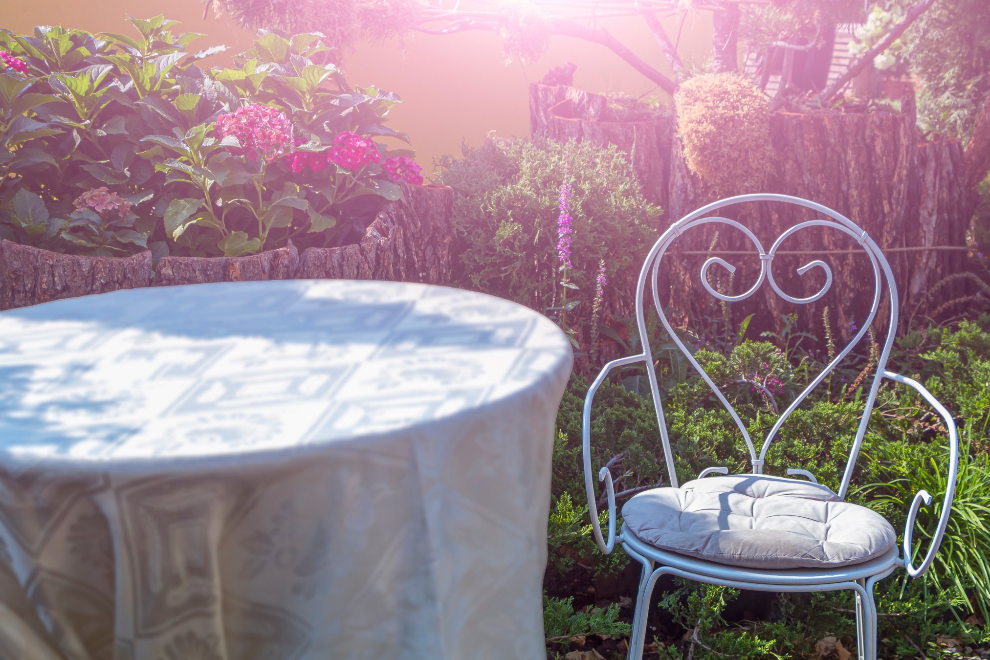 White metal iron chair and table outdoors. Retro styled furniture in magic green summer garden, symbols of Alice in Wonderland.